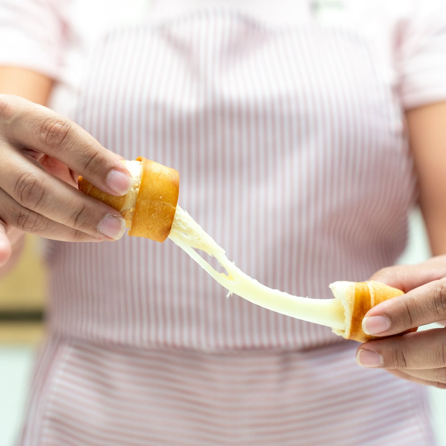 Tequeño recién frito partido a la mitad, con el queso estirándose entre las dos mitades.